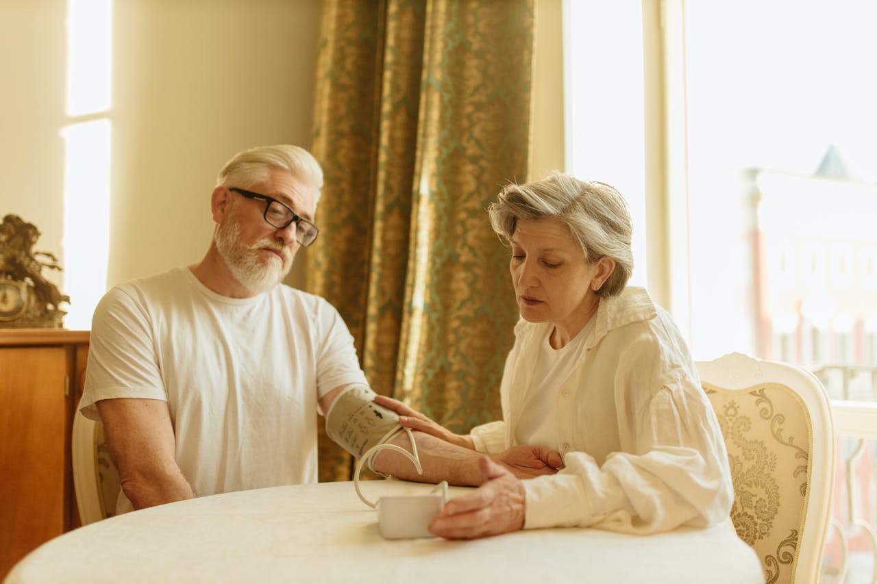 An elderly couple at home measuring blood pressure with a digital monitor, depicting care and health awareness.